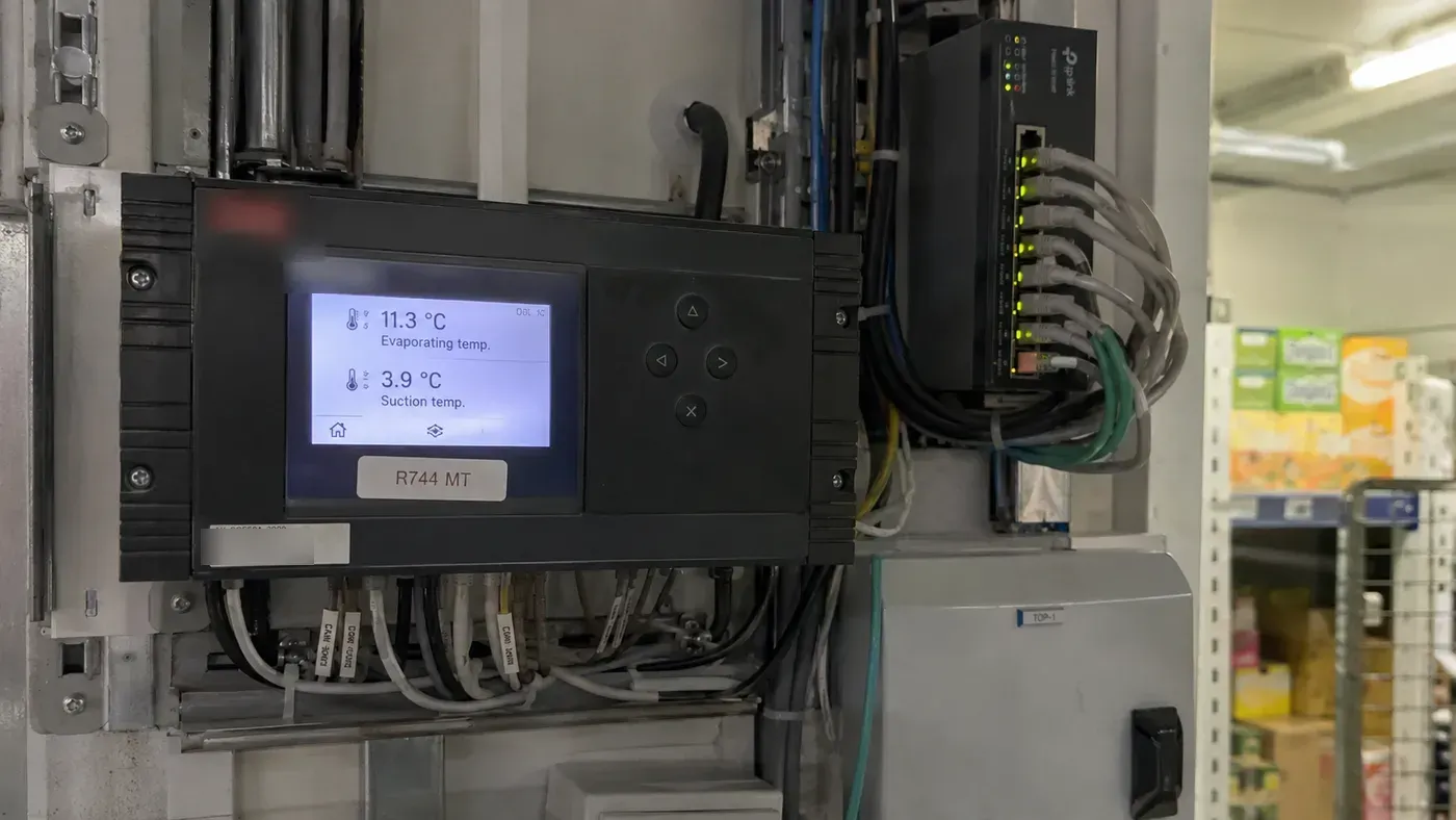 A wall-mounted refrigeration controller and connected network switch in a supermarket storeroom (illustration)