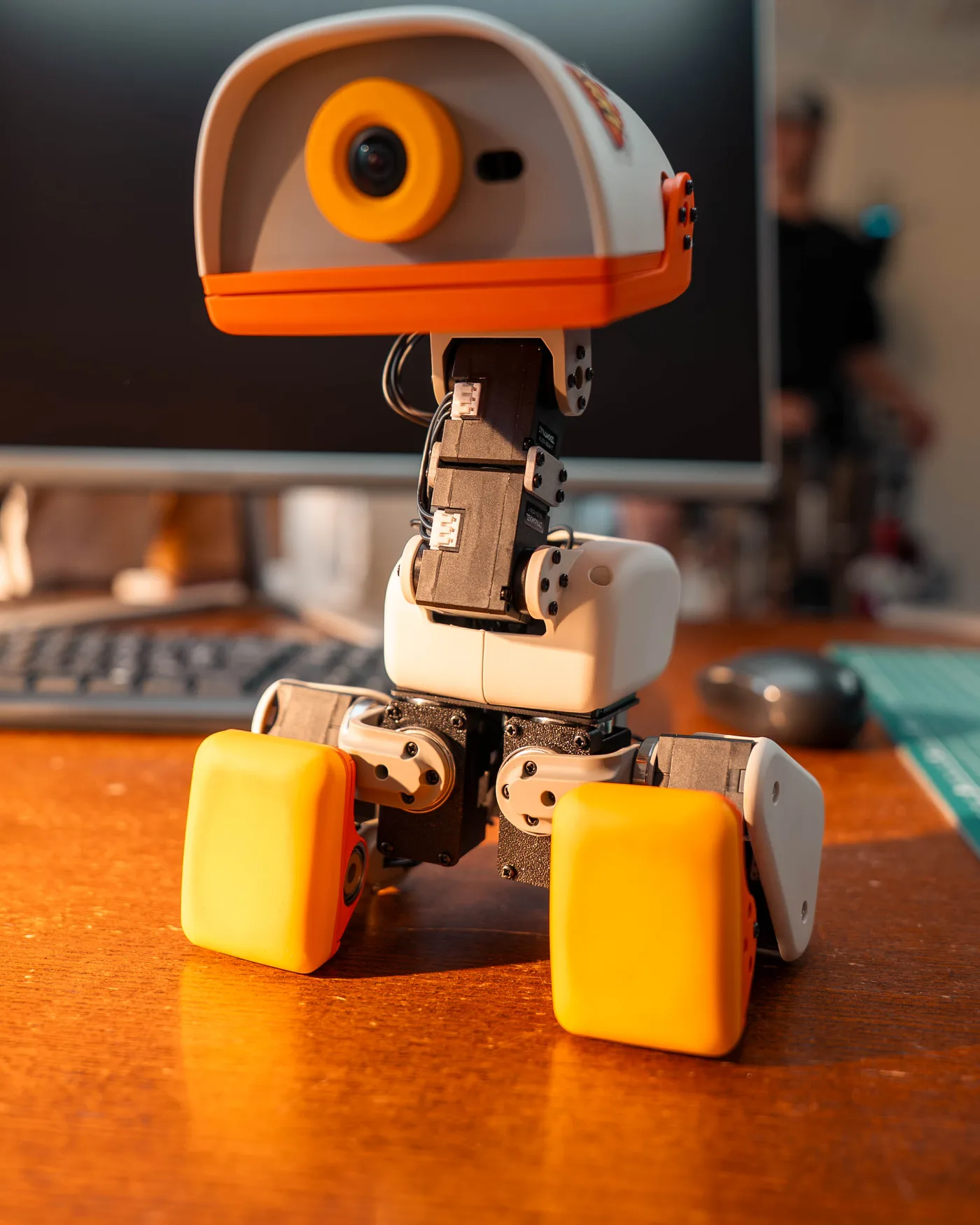 A Microduck robot duck standing on a desk in front of a computer screen
