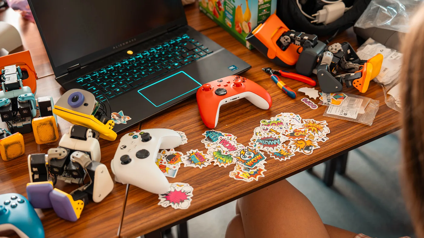 Microduck parts, game controllers, a laptop and stickers spread out on a table