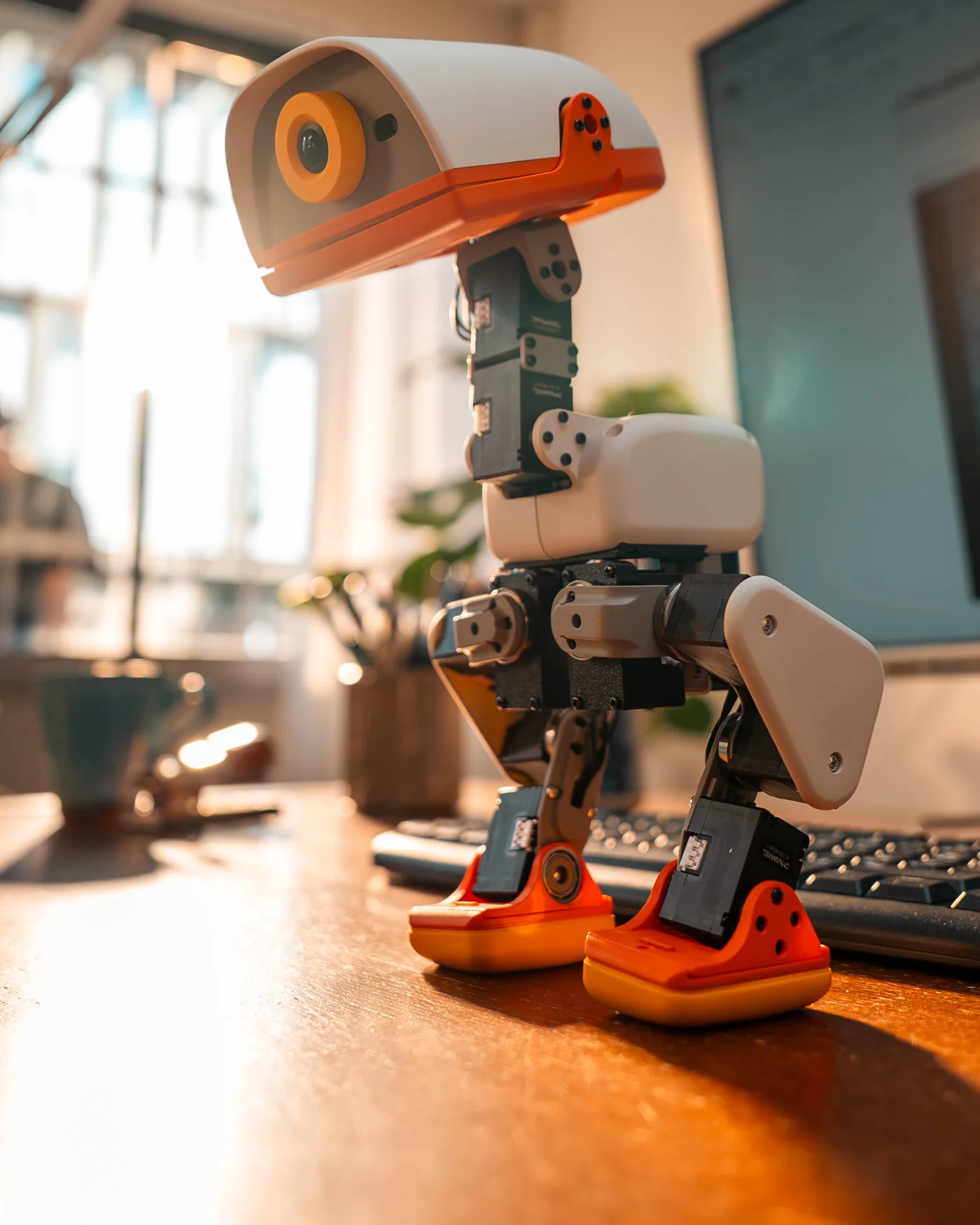 Close-up of an orange and white Microduck robot duck on a desk, showing its legs, motors and camera eye