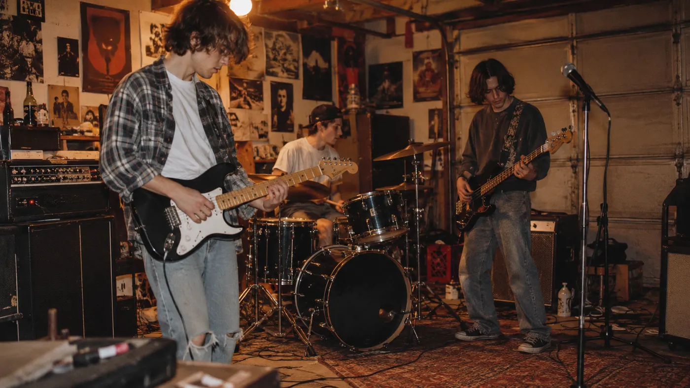 A three-piece grunge band rehearsing in a garage covered in posters (illustration)